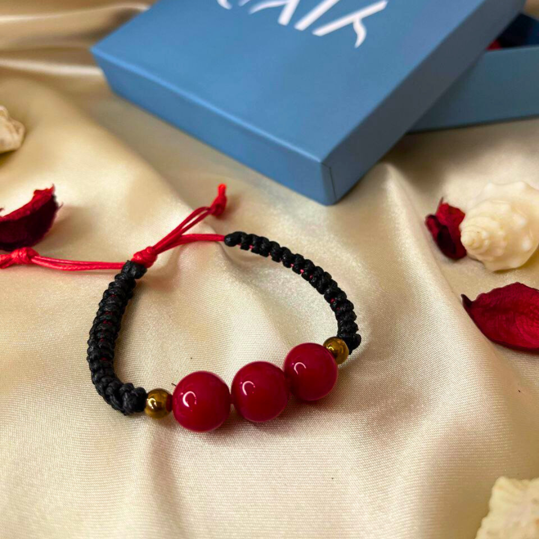 Bracelet with red beads and black cord on a beige fabric background with a blue box.