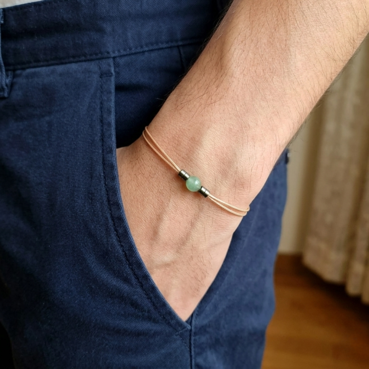 Close-up of a wrist wearing a bracelet with a green bead, against a blurred background.
