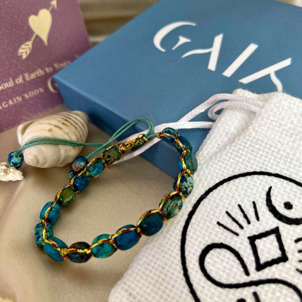 Bracelet with blue and gold beads on a white surface with a book and card in the background.