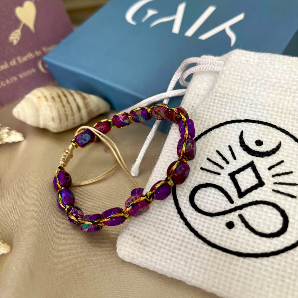 Beaded earrings on a white drawstring bag with a logo, next to a blue box and book.