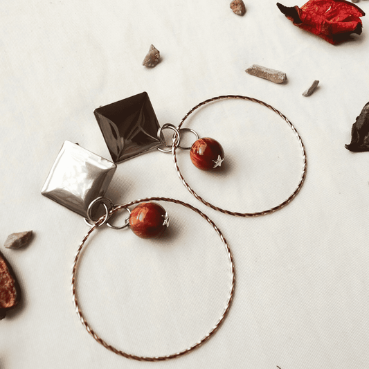 Pair of hoop earrings with geometric and round pendants on a neutral background