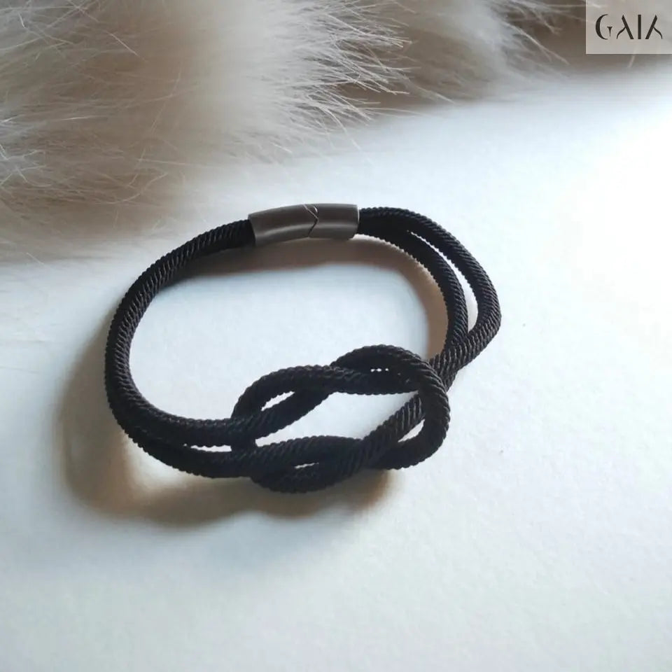 Black knotted bracelet on a white surface with fur in the background