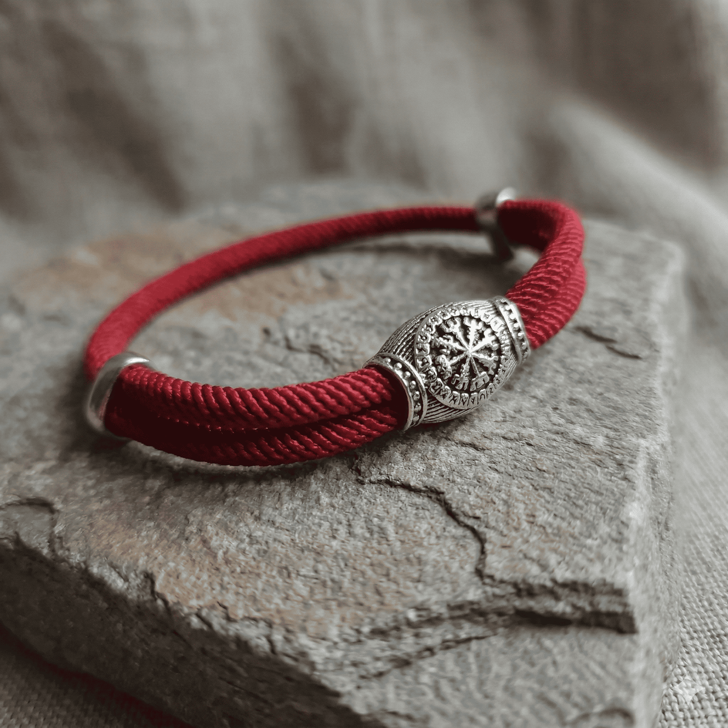 Red bracelet with a silver decorative clasp on a stone surface