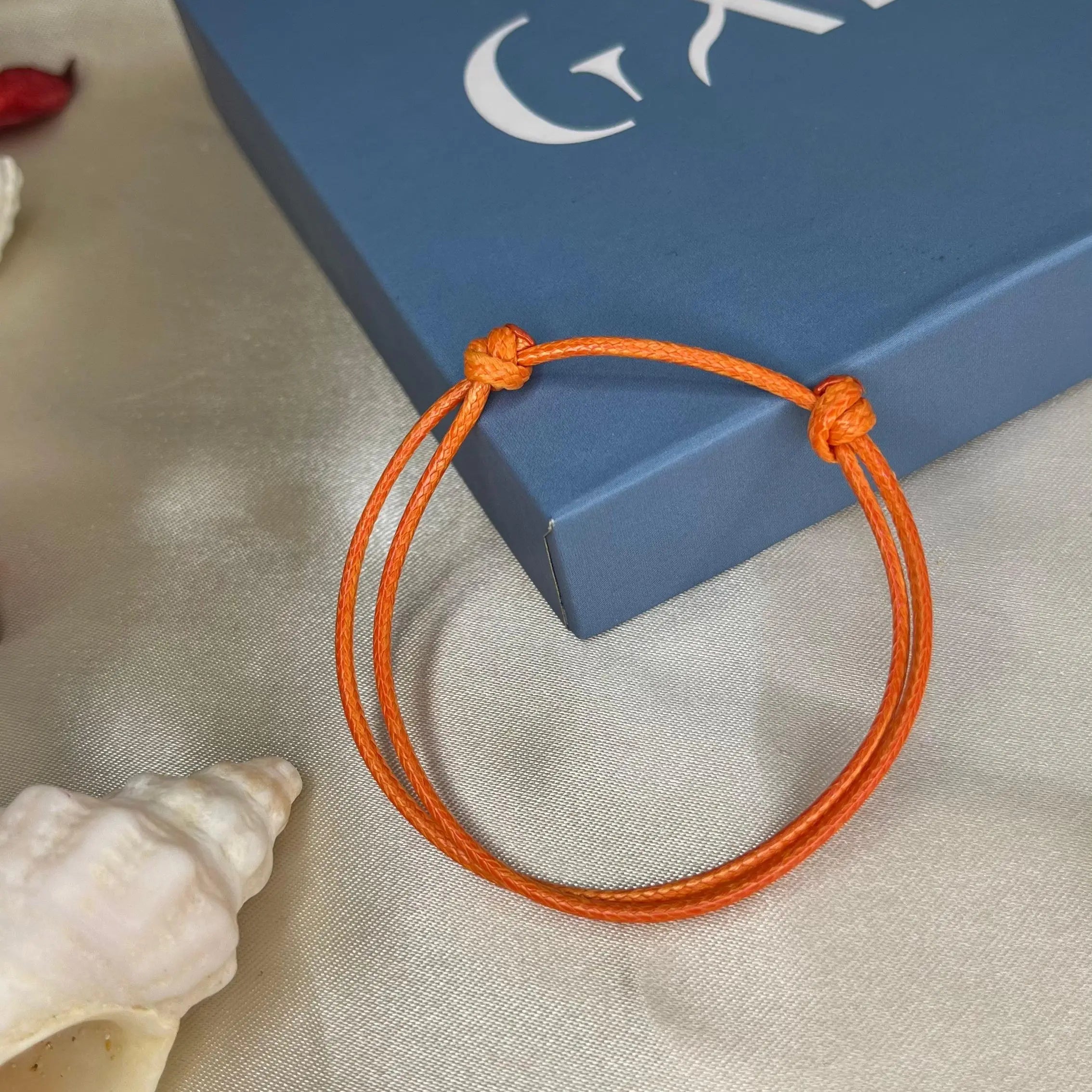 Orange bracelet on a light surface with a blue box featuring 'GAIK' branding.