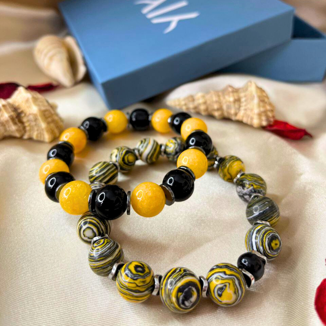 Set of beaded bracelets with yellow, black, and gray beads on a beige surface with a blue box in the background.