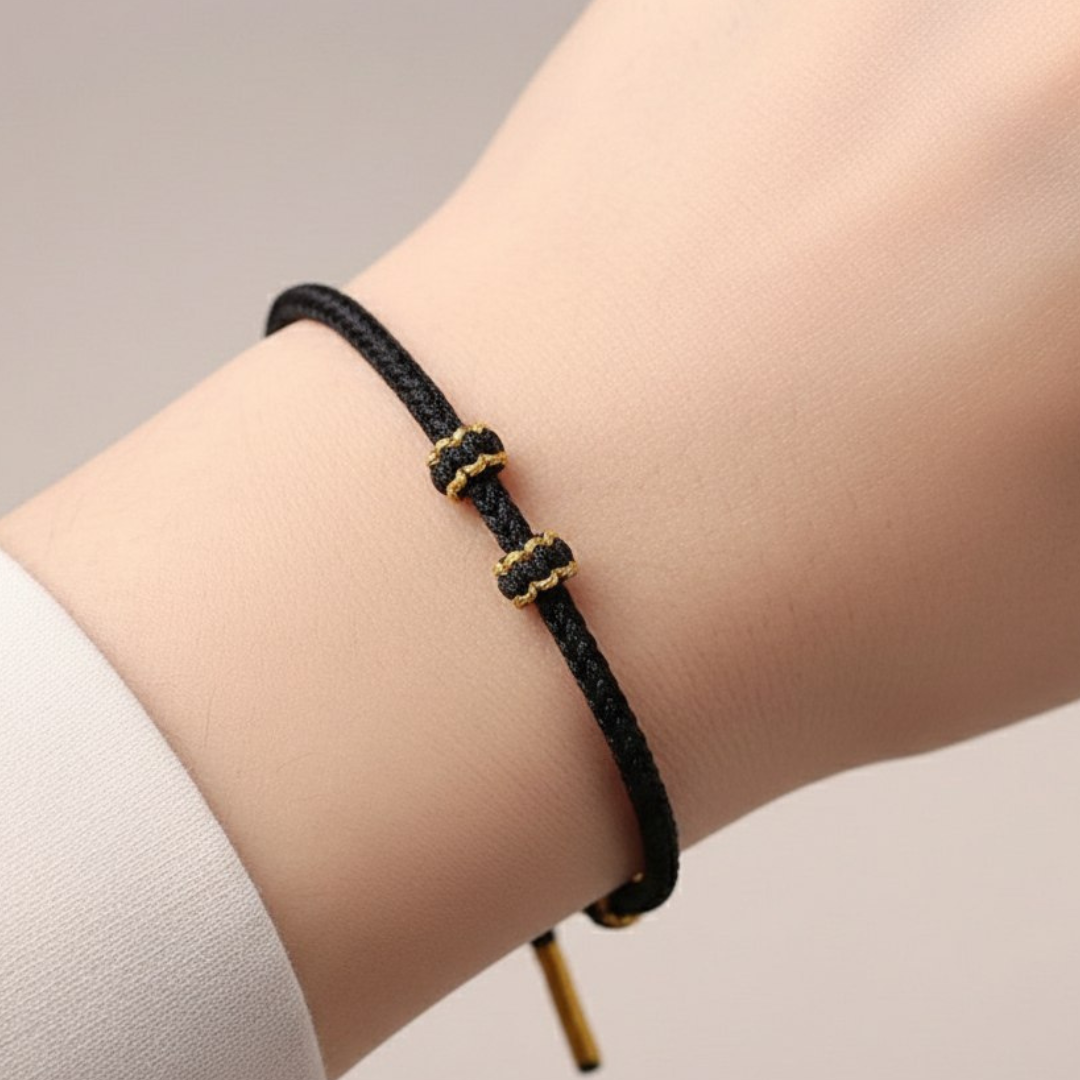 Black braided bracelet with gold accents on a wrist against a neutral background