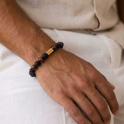 Hand wearing a beaded bracelet with a visible brand name on a neutral background