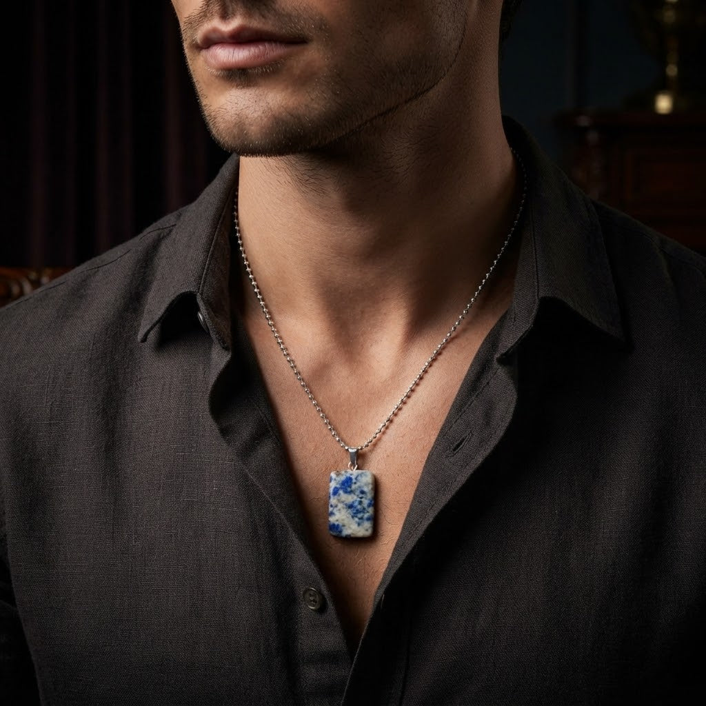 A close-up of a man wearing a silver chain necklace with a rectangular pendant featuring a blue and white marbled pattern, styled with a dark charcoal button-down shirt.