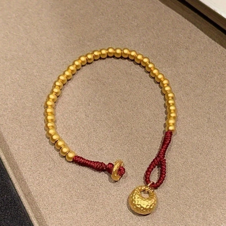 Gold beaded bracelet with a red string on a beige surface