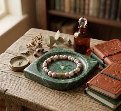 Bracelet on a green stone dish with books and a bottle on a wooden table