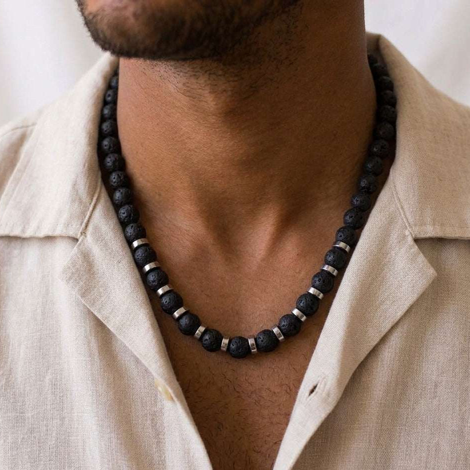 Man wearing a black beaded necklace with a beige shirt against a neutral background