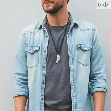 Man wearing a light blue denim jacket, gray t-shirt, black jeans, and black sneakers against a light gray wall.