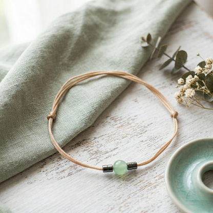 Bracelet with a green bead on a wooden surface with a cloth and small plant