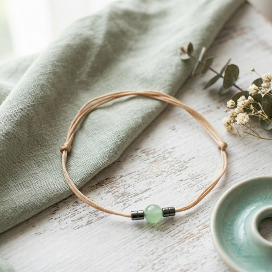 Bracelet with a green bead on a wooden surface with a cloth and small plant