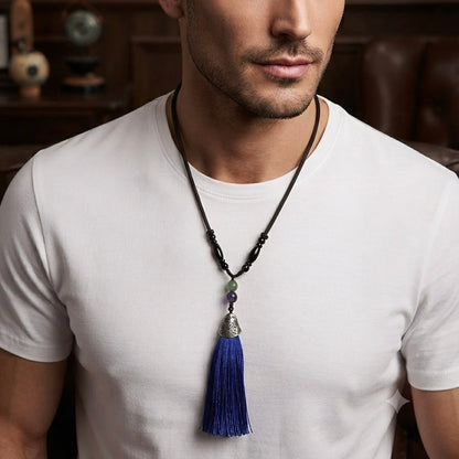 Man wearing a black cord necklace with a long blue tassel pendant and decorative beads.