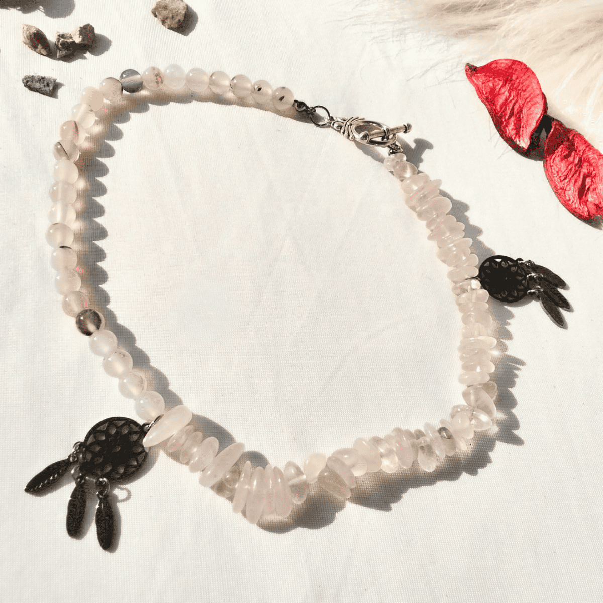Necklace with pink beads and black dreamcatcher charm on a white shell background
