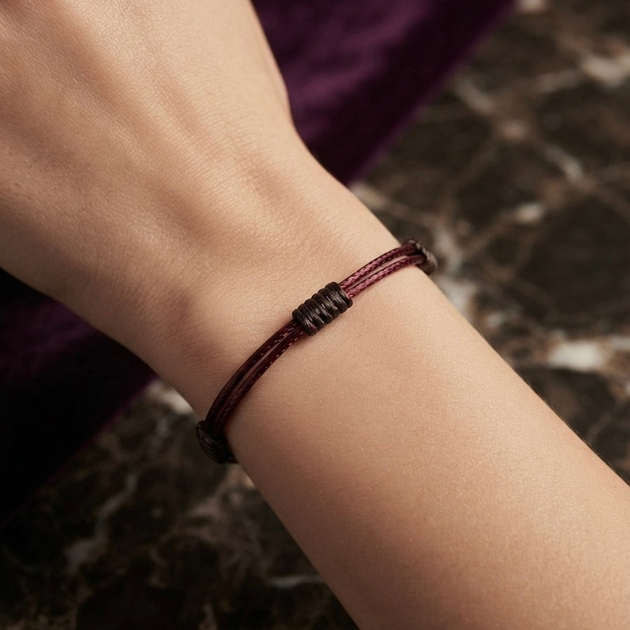Wrist wearing a minimal burgundy cord bracelet with dark wrapped knot details.