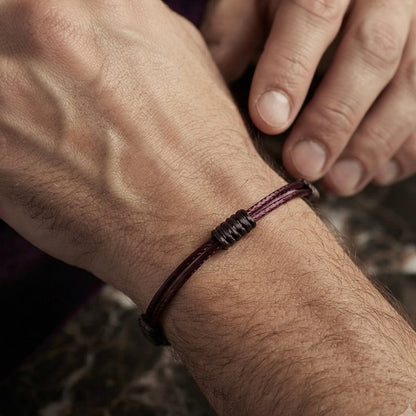Man wearing a minimal burgundy cord bracelet with dark wrapped knot details.