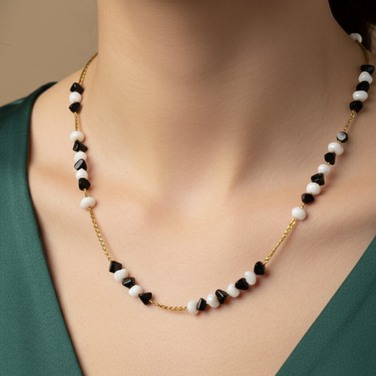 Necklace with black, white, and gold beads on a person wearing a green top.
