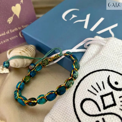 Bracelet with blue and gold beads on a white surface with a book and card in the background.