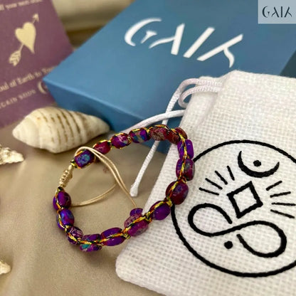 Beaded earrings on a white drawstring bag with a logo, next to a blue box and book.