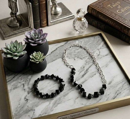 Black beaded bracelet and necklace on a marble tray with decorative items.