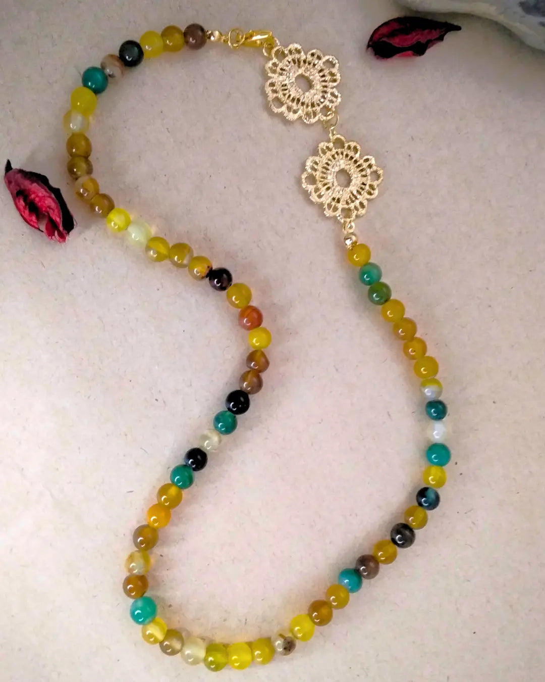 Colorful beaded necklace with gold floral clasp on a light background