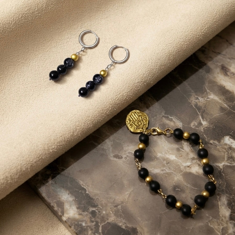 A jewelry set featuring a pair of drop earrings and a matching bracelet. The jewelry has dark navy blue beads, polished gold spacer beads, silver-toned metal rings, and a round gold-toned medallion charm.