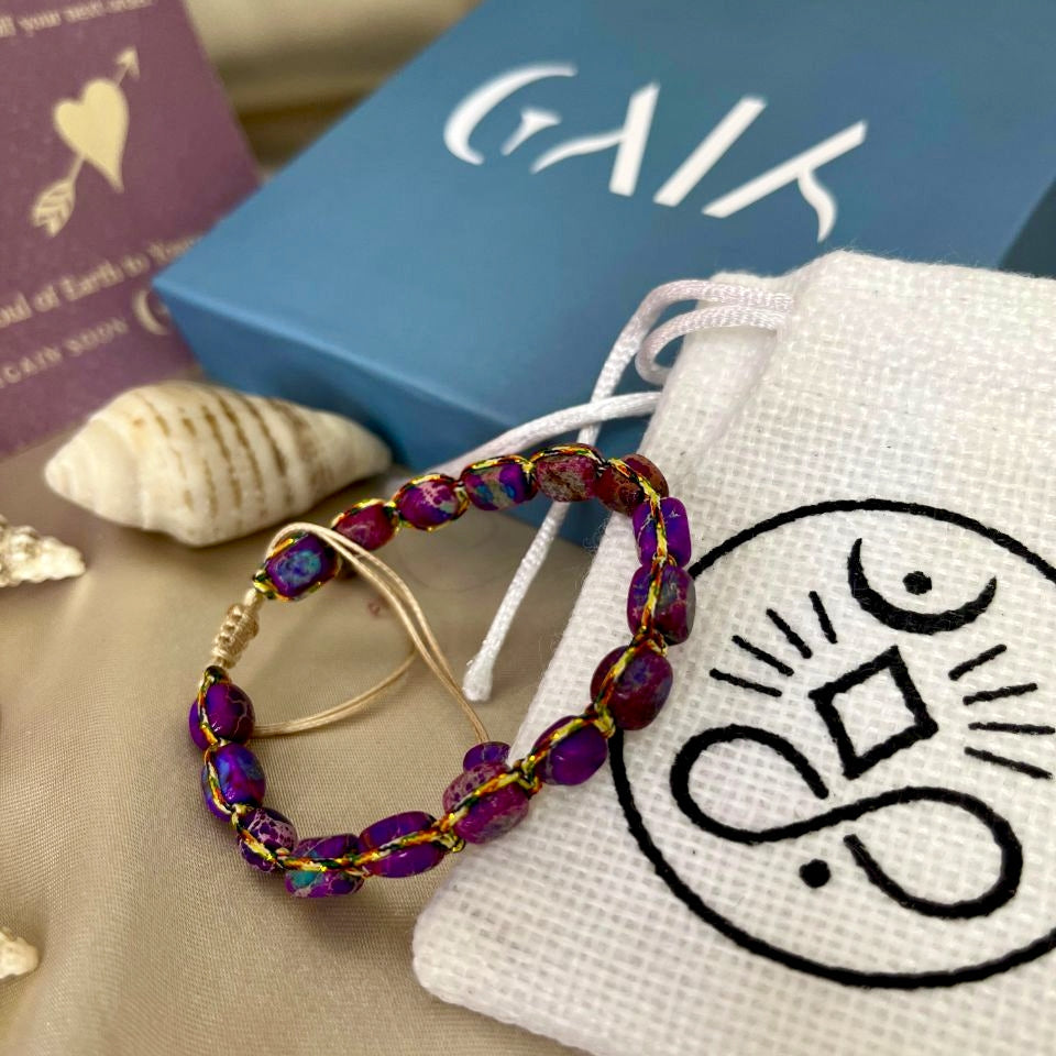 Beaded earrings on a white drawstring bag with a logo, next to a blue box and book.