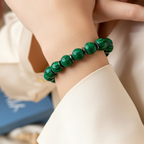 Close-up of a hand wearing a green beaded bracelet with a blurred background