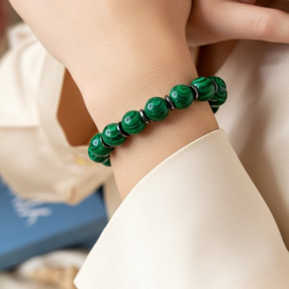 Close-up of a hand wearing a green beaded bracelet with a blurred background