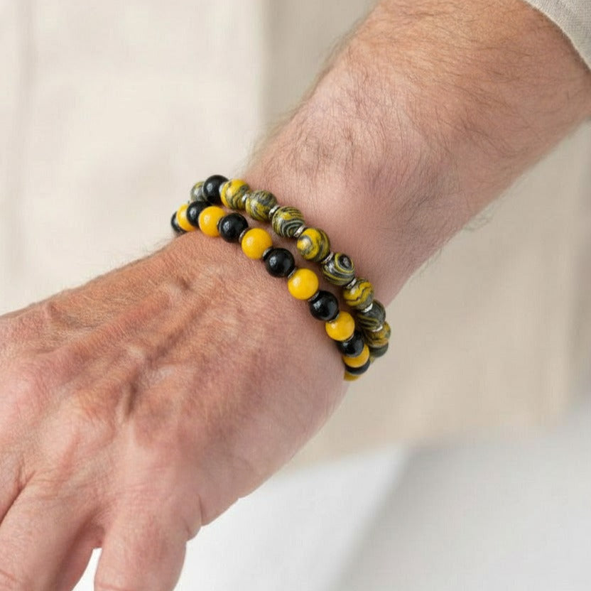 Close-up of a wrist wearing a bracelet with yellow and black beads on a plain background