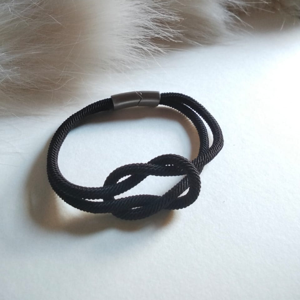 Black knotted bracelet on a white surface with fur in the background