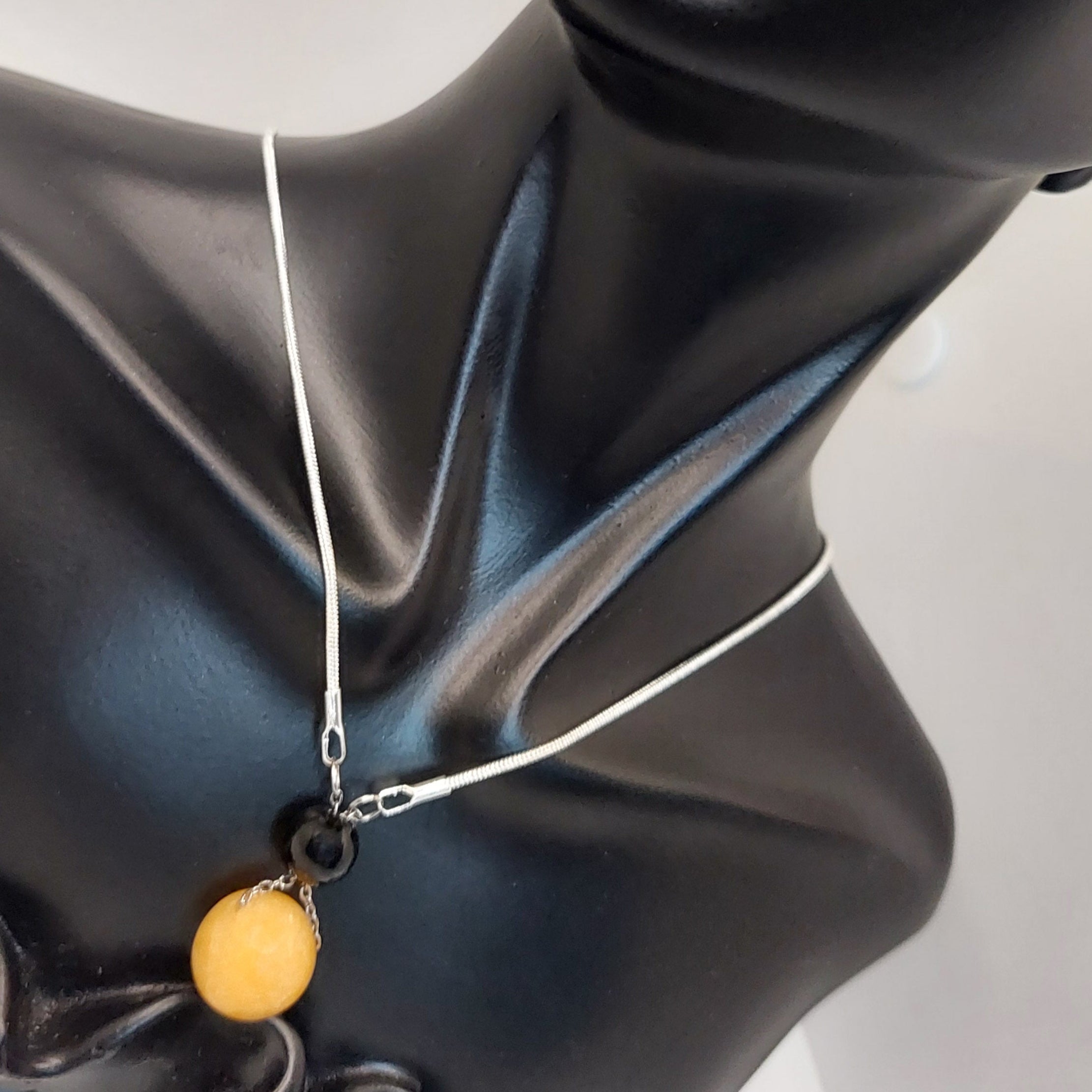 Black bust wearing a necklace with a yellow pendant on a white background

