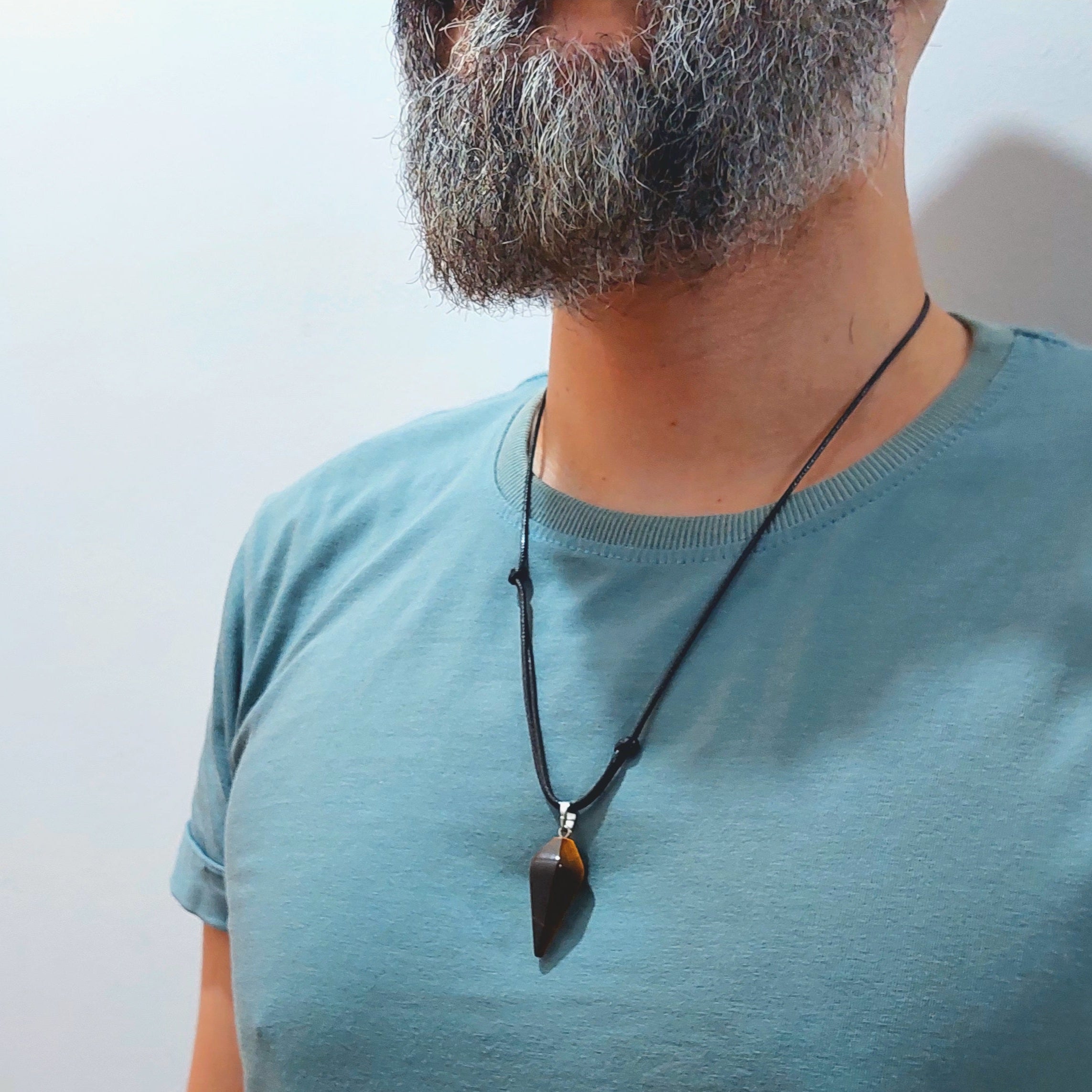 Man wearing a light blue t-shirt with a necklace against a white background