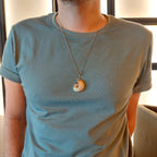Person wearing a light blue t-shirt with a  gaia necklace featuring a circular pendant.