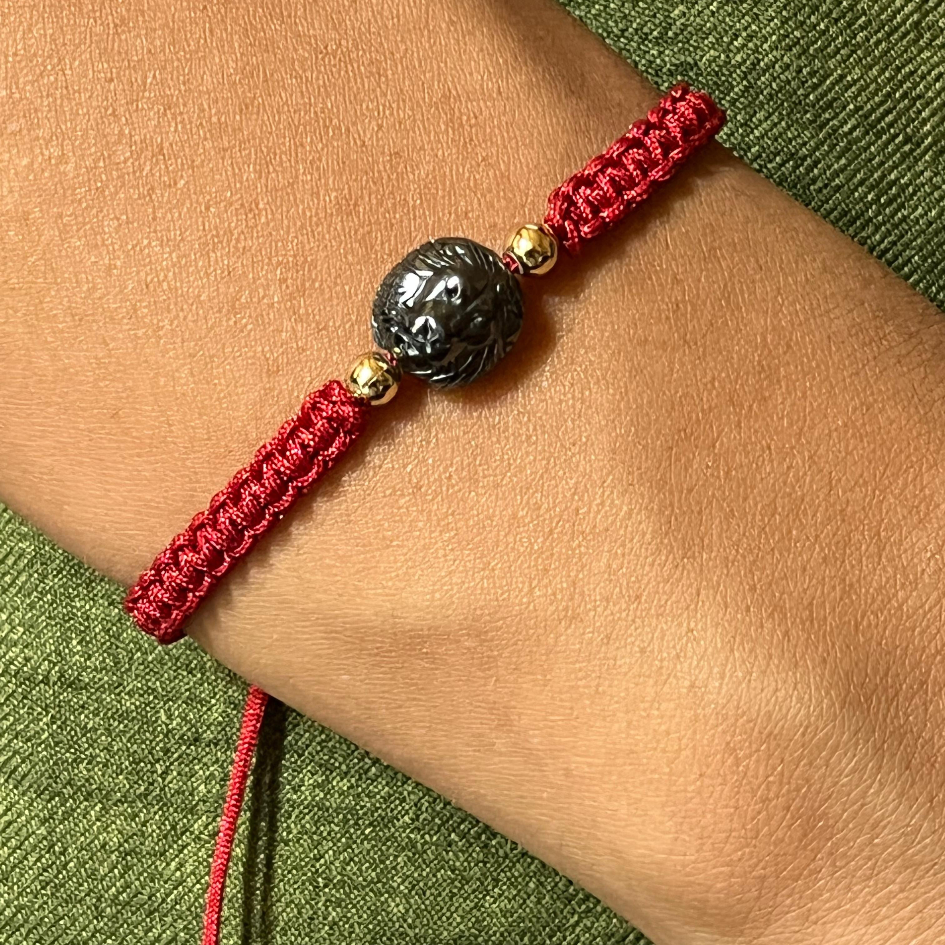 Red bracelet with a black and gold bead on a wrist against a green fabric background