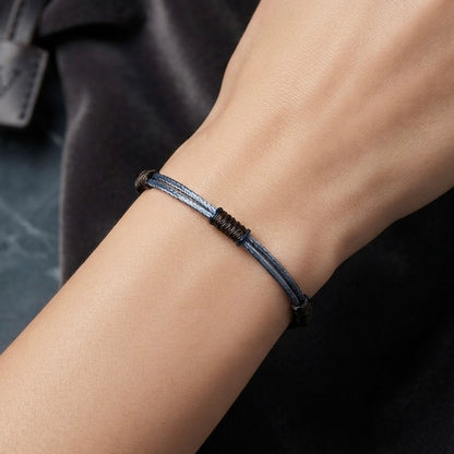 Wrist wearing a minimal grey cord bracelet with black wrapped knot details.