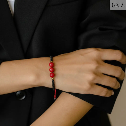 Person wearing a black blazer with a red beaded bracelet on a neutral background