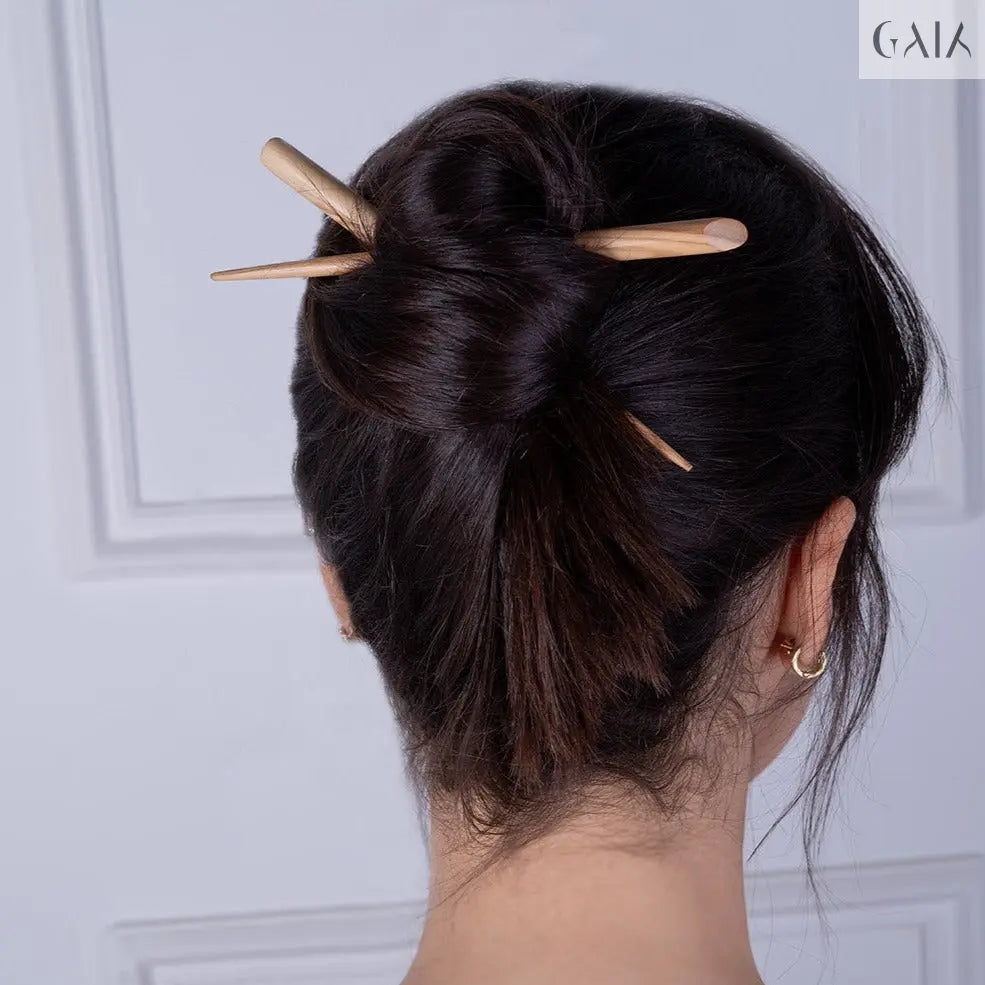 Dark brown hair styled in a bun secured with a hand-carved olive wood hair stick with a smooth finish