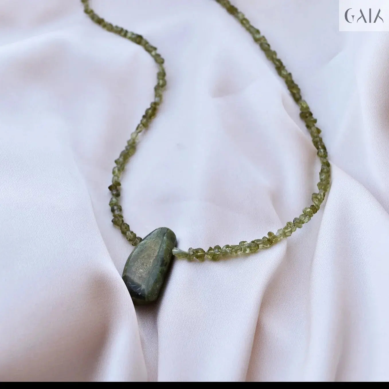 Handcrafted Hope Necklace featuring natural green tourmaline centerpiece and peridot beads on soft white fabric background.