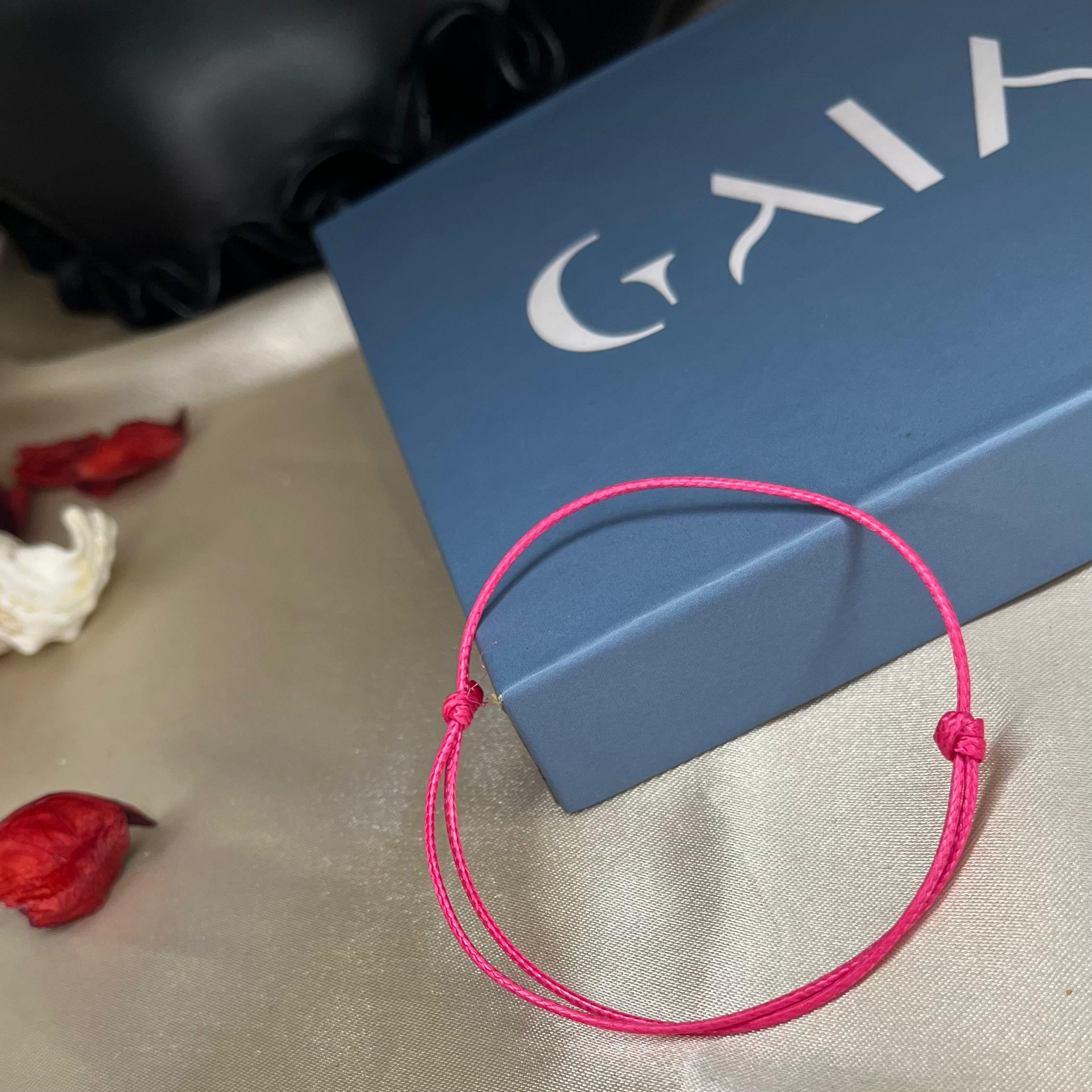Pink bracelet on a textured surface with a blue box labeled 'GAIA' in the background.