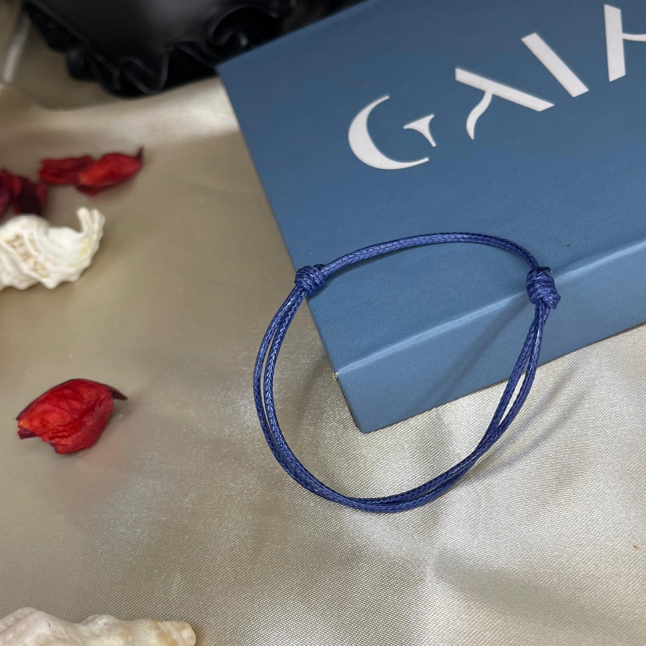 Blue bracelet on a white surface with a black container and red objects in the background
