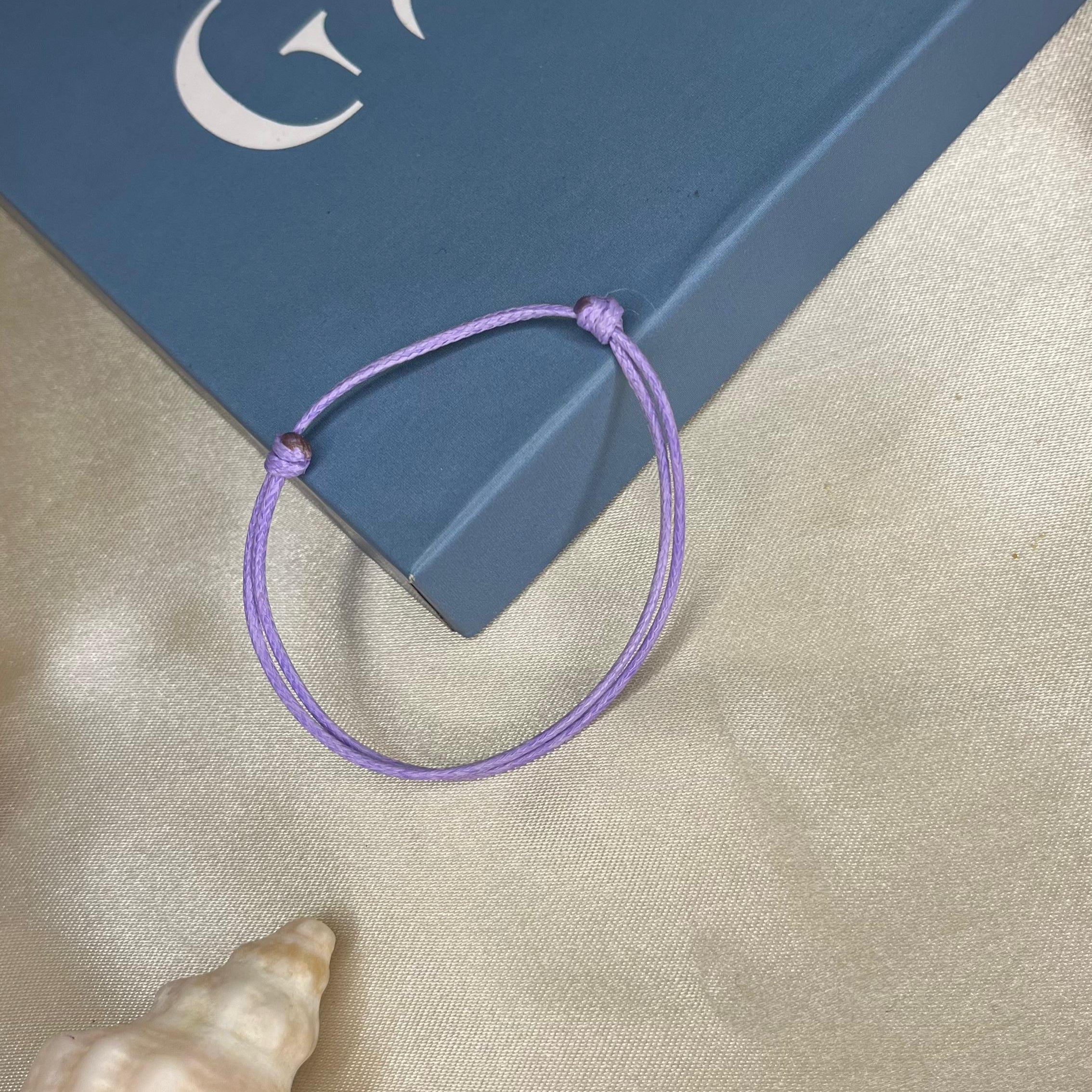 Purple bracelet on a blue box with 'GALA' branding, next to a shell on a beige surface.