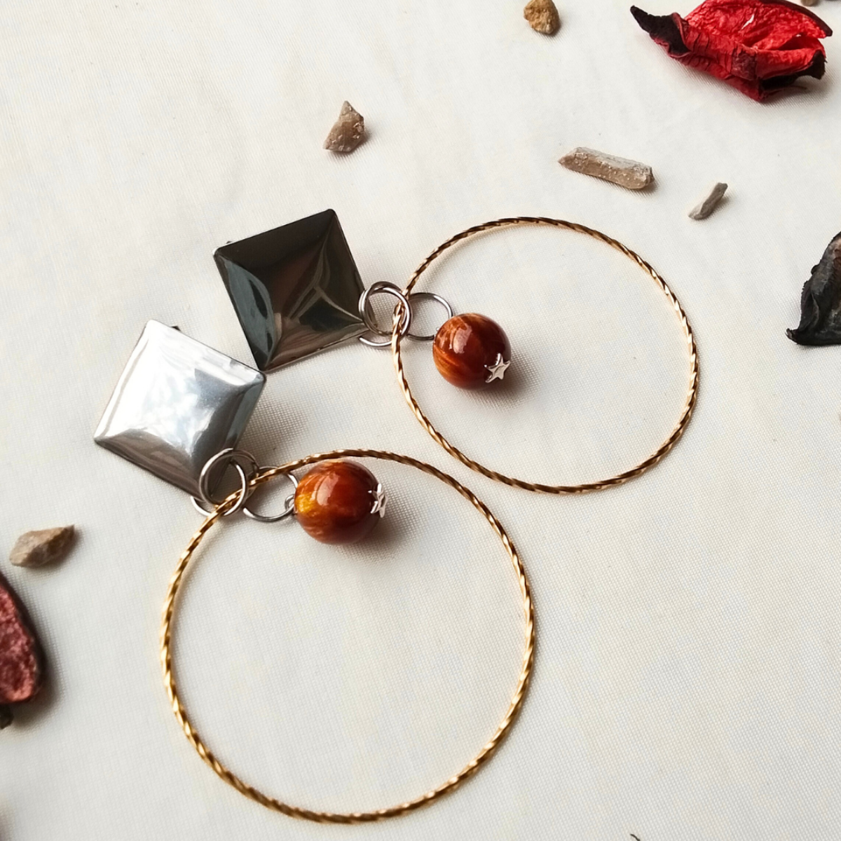 Pair of hoop earrings with geometric and round pendants on a neutral background