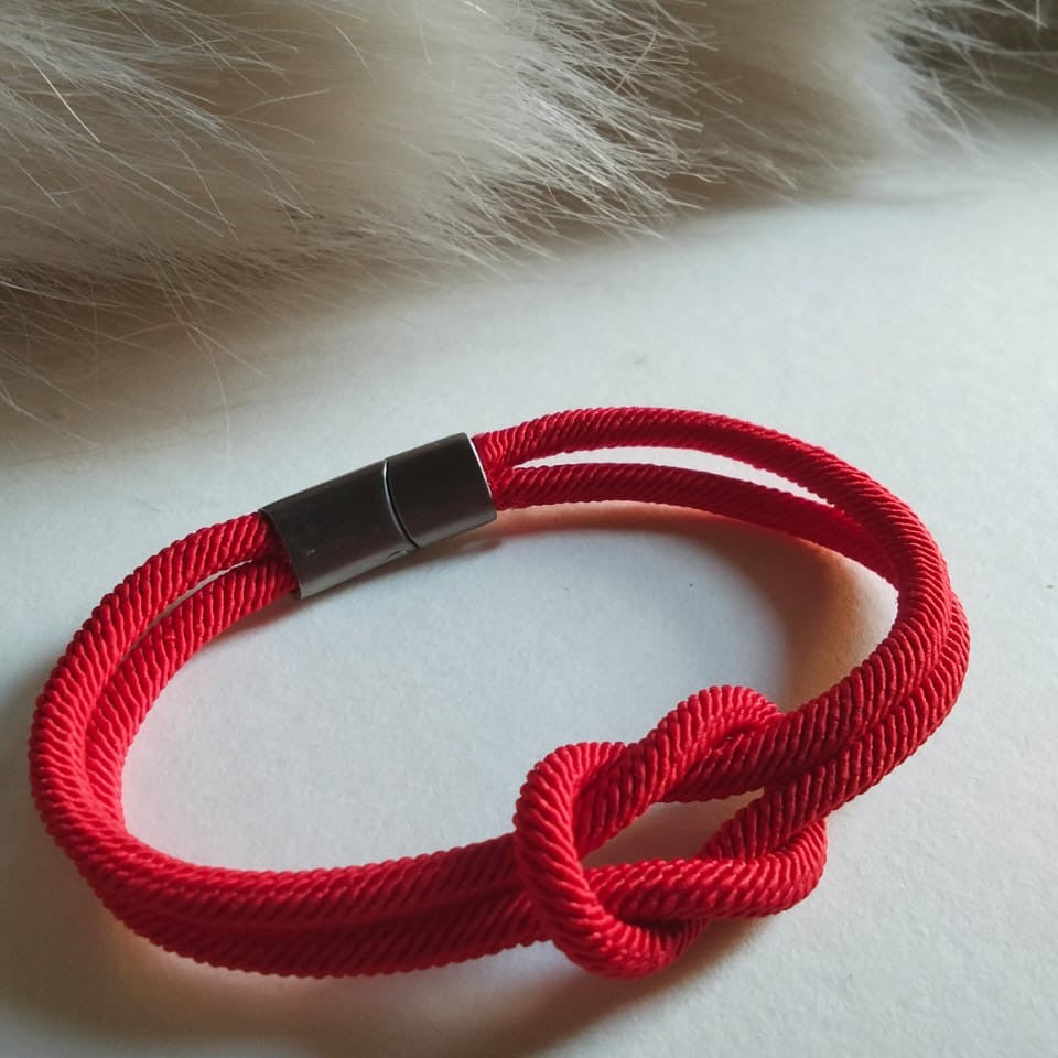 Red rope bracelet with a knot on a white surface