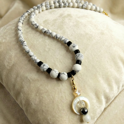 Necklace with white, black, and gold beads on a beige fabric background