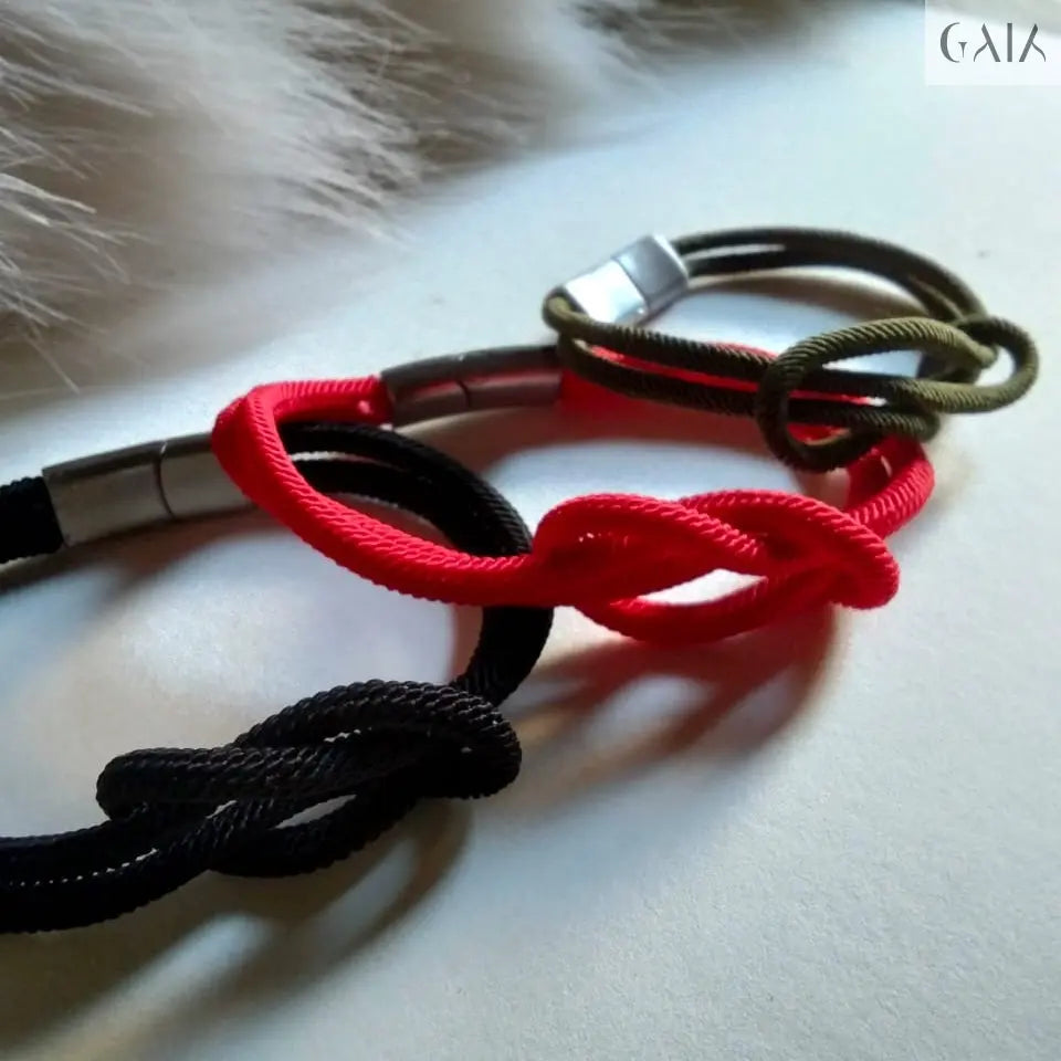 Three braided bracelets in black, red, and green on a textured surface.