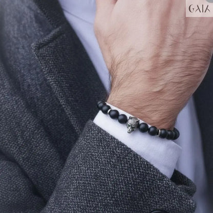 Person wearing a black beaded bracelet with a silver charm on a gray background