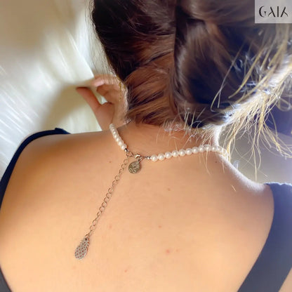 Pearl necklace with a silver chain and pendant on a person's neck.